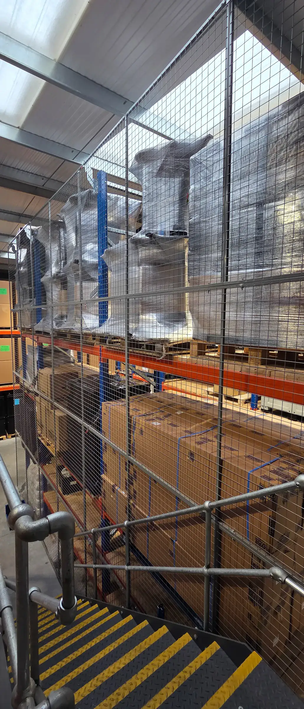 Anti-collapse mesh on pallet racking beside mezzanine stairs