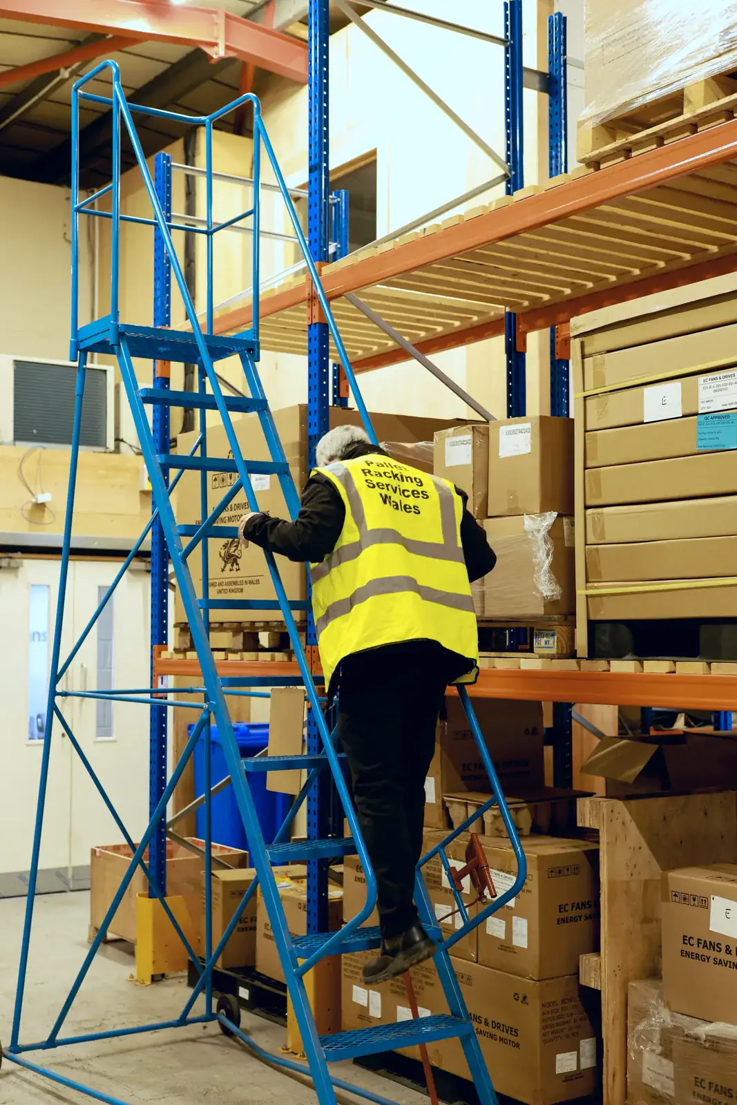 Team member on mobile safety steps checking stock on pallet racking