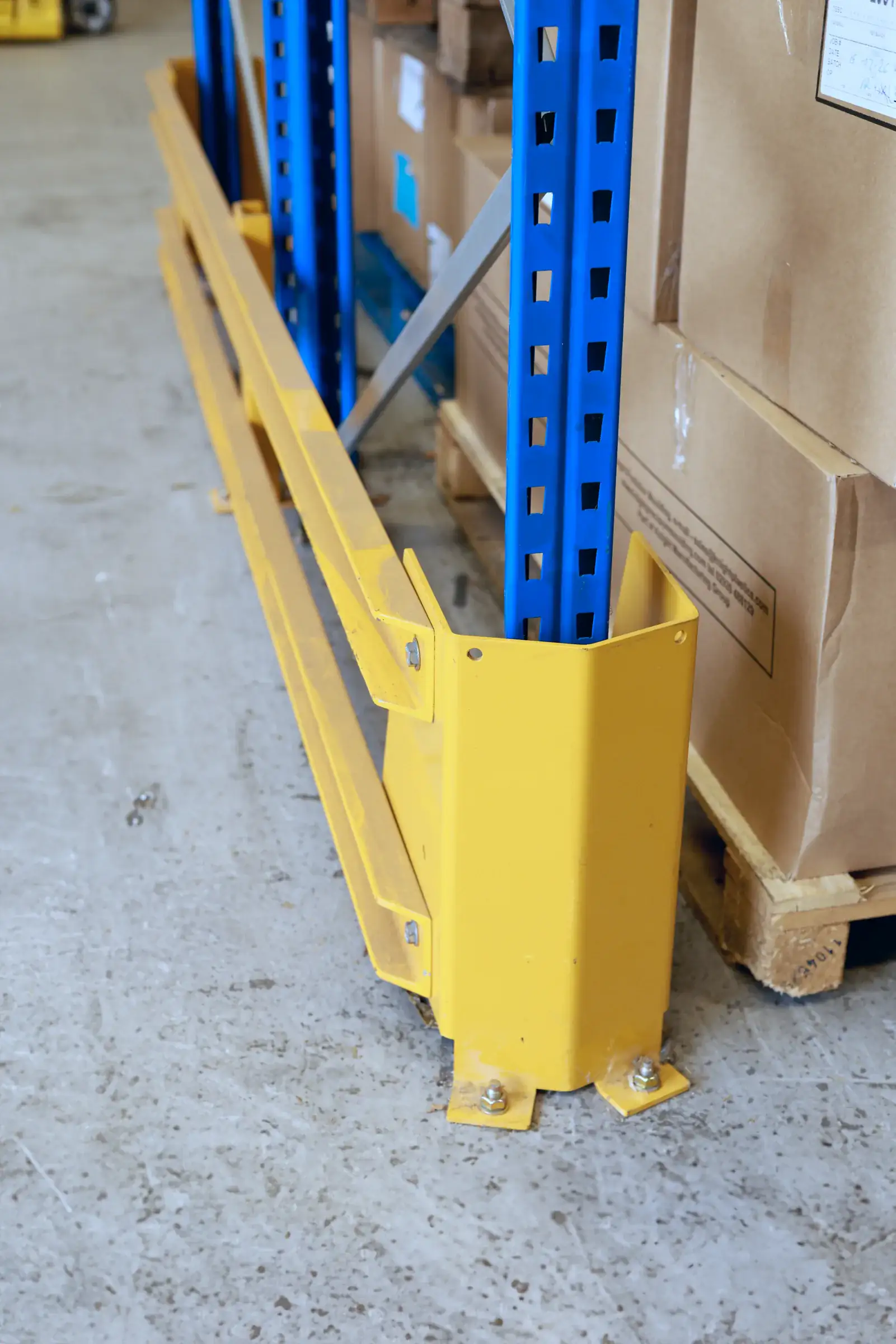 Upright protector and barrier rail at the base of pallet racking
