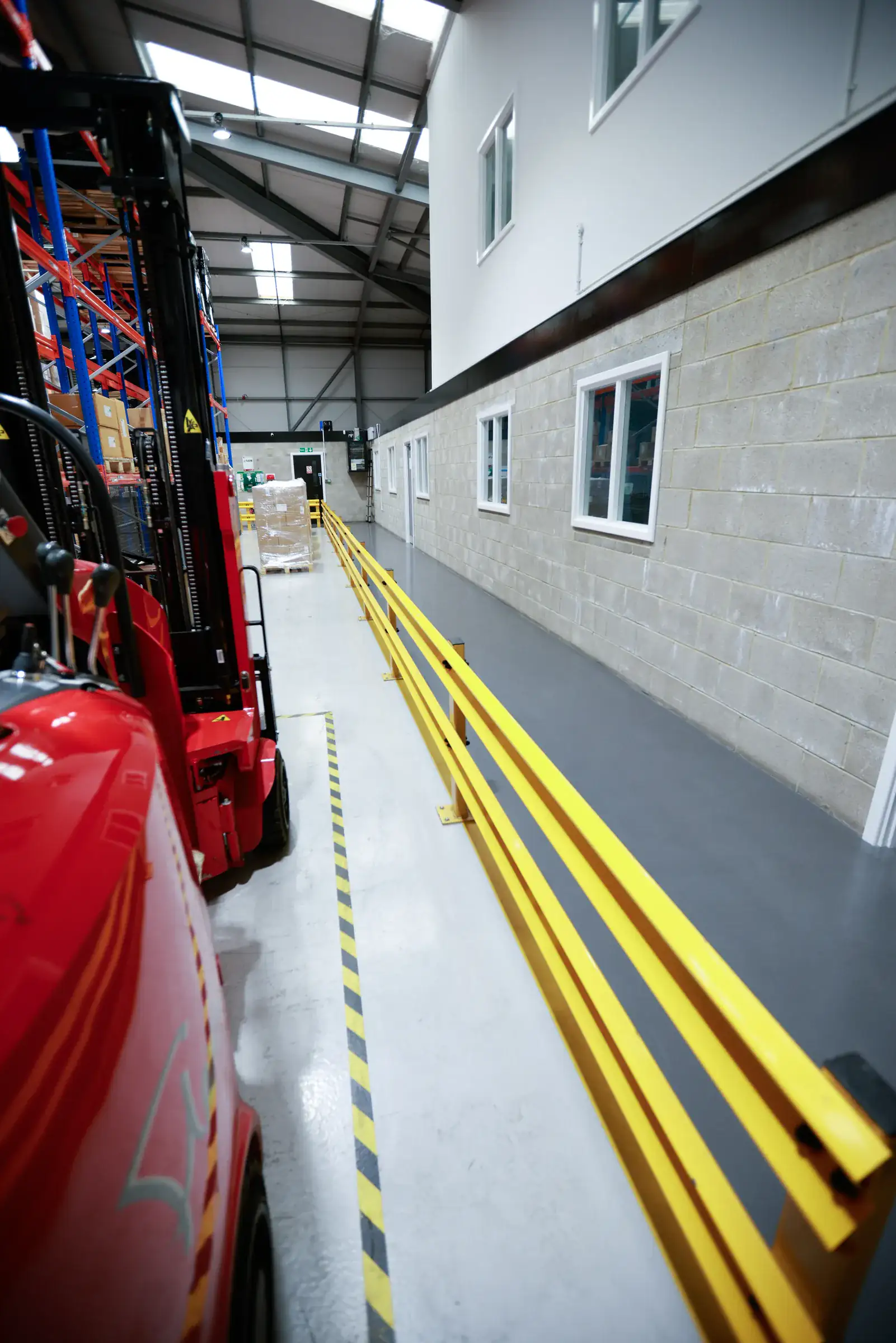 Yellow pedestrian barrier rail along a warehouse wall with a forklift